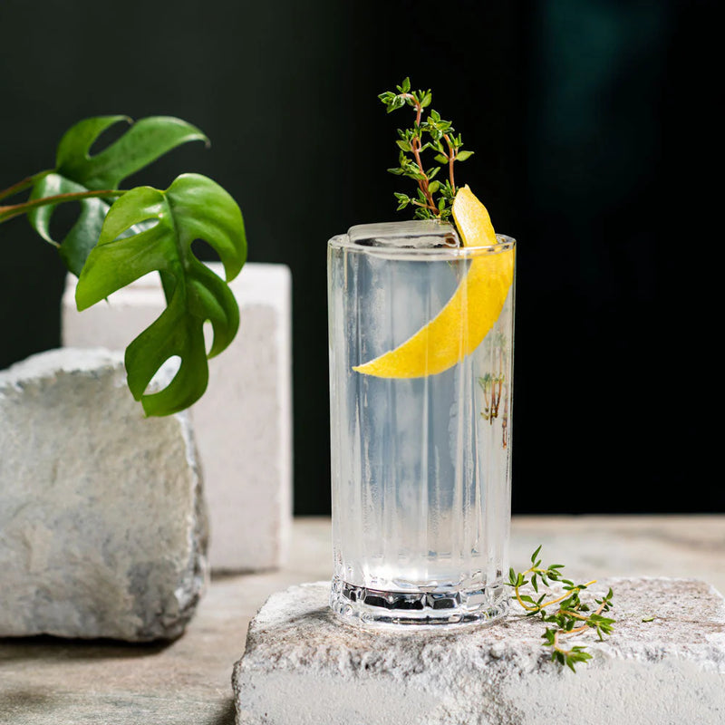 A refreshing Tom Collins cocktail with lemon peel and thyme garnish in a highball glass.