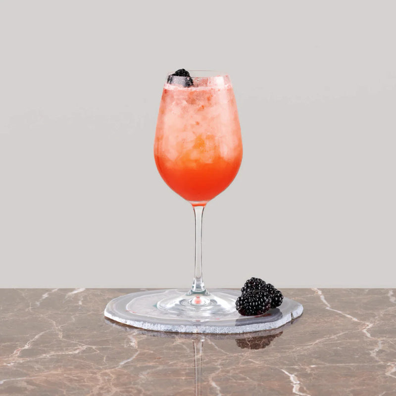 Refreshing Ostend Fizz cocktail served in a wine glass with ice and blackberries on a marble surface.