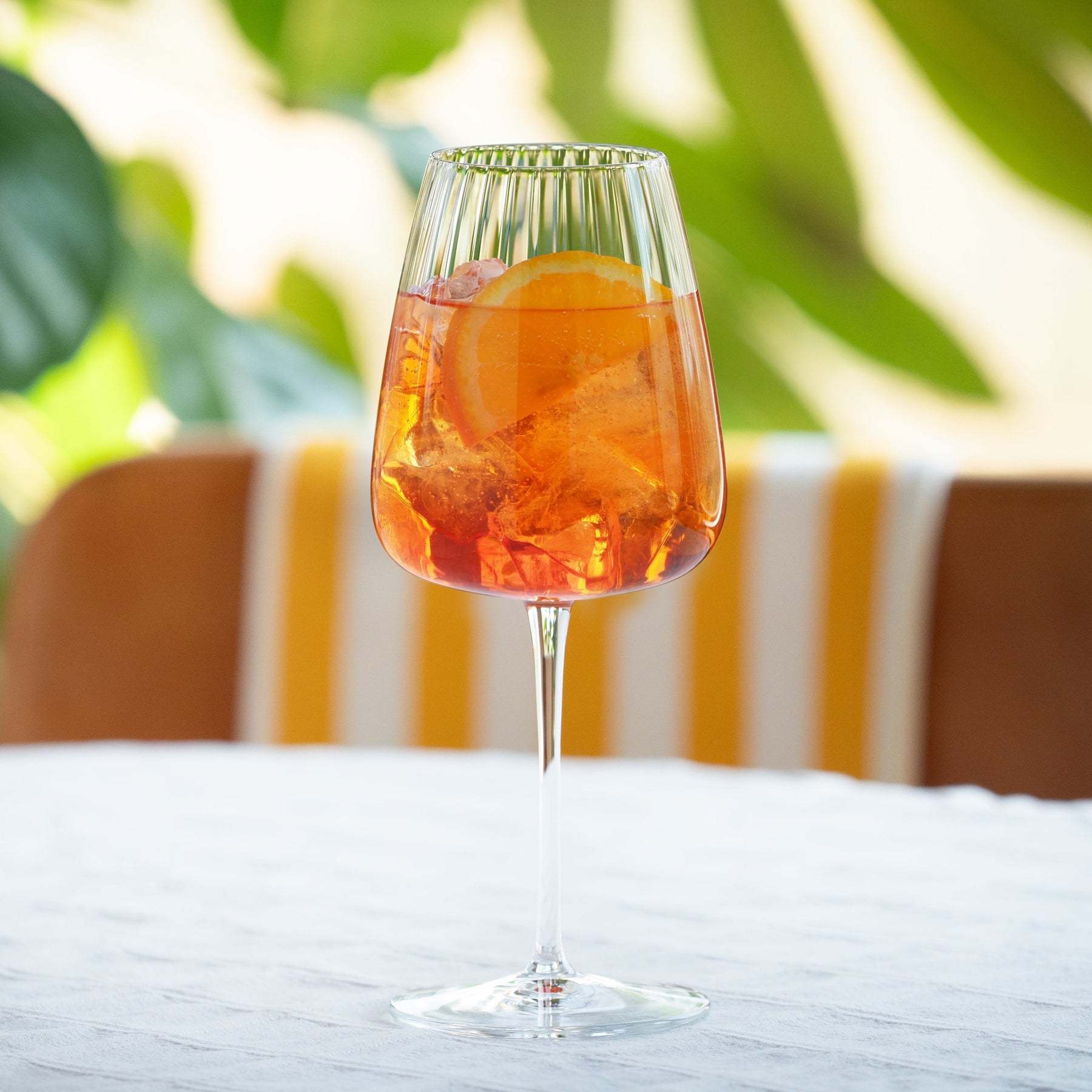 Glass of Aperiniets Spritz Royale on table, showcasing aperiniets spritz cocktail recipe with orange slice on a sunny day.