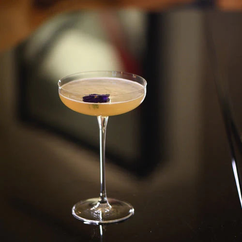 Cuban Twist cocktail served in a stylish glass with a purple flower garnish, reflecting elegance and flavor.