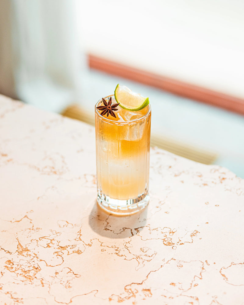 A refreshing Dark & Stormy cocktail garnished with a lime slice and star anise, displayed on a stylish table.