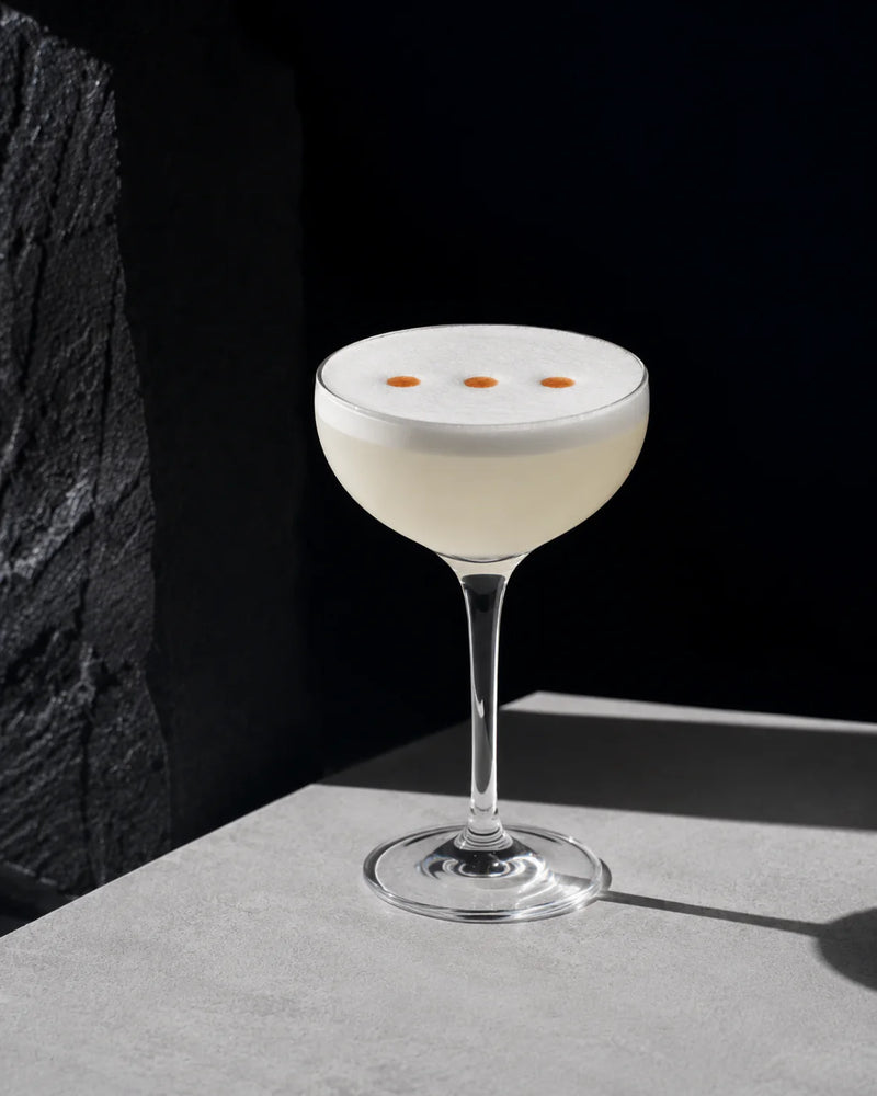 A beautifully crafted Dry & Sour cocktail with frothy foam and orange accents in an elegant glass.