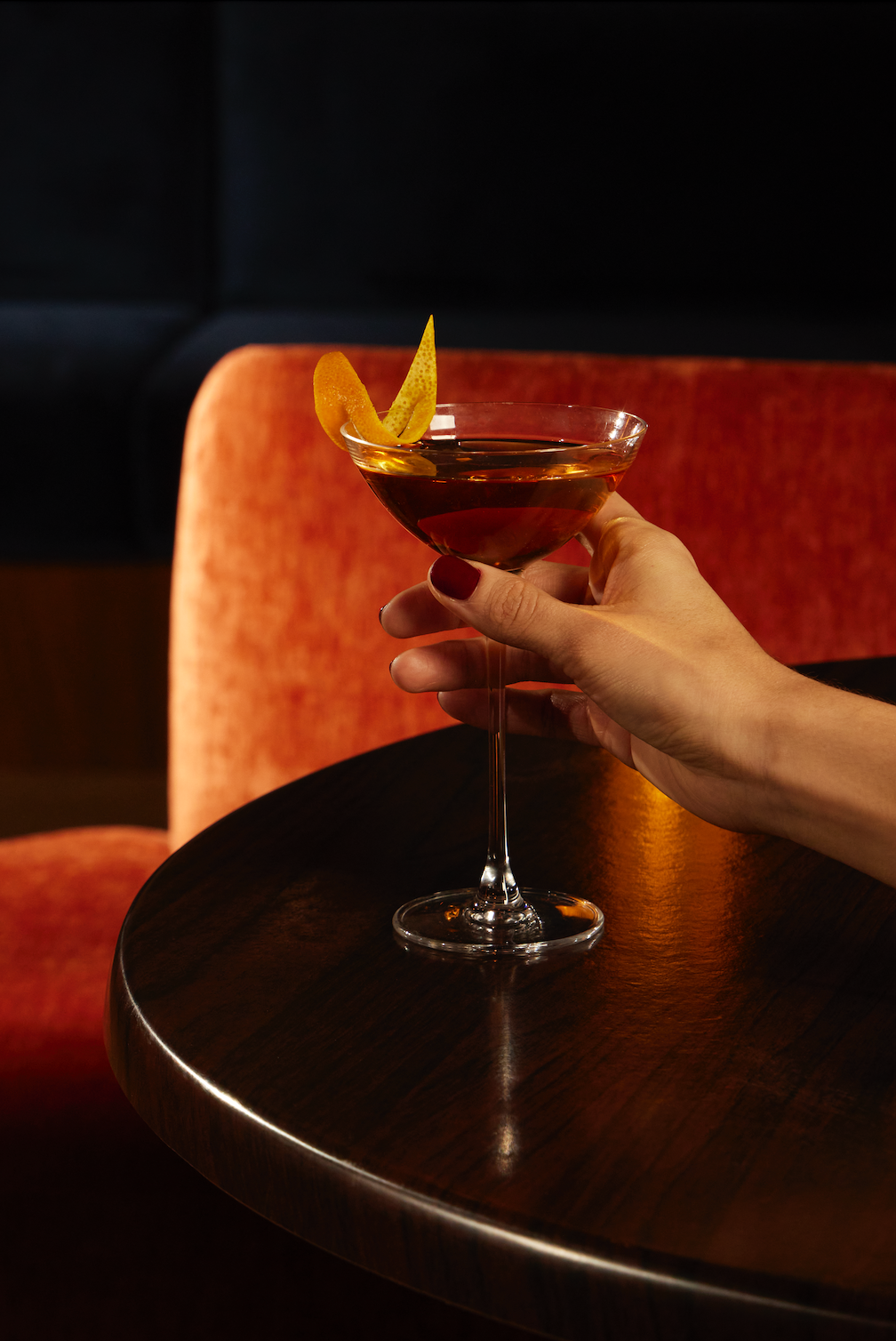 Hand holding a glass of non-alcoholic daiquiri recipe garnished with citrus peel, set against an elegant cafe atmosphere.