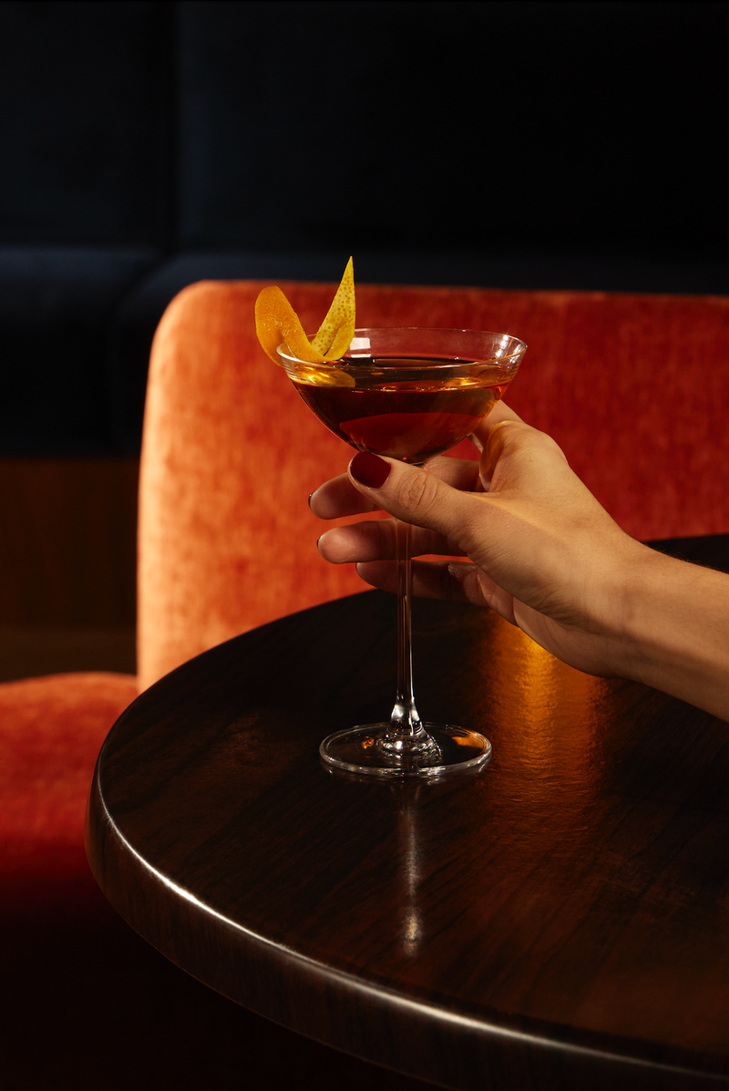 Hand holding a glass of non-alcoholic daiquiri recipe garnished with citrus peel, set against an elegant cafe atmosphere.