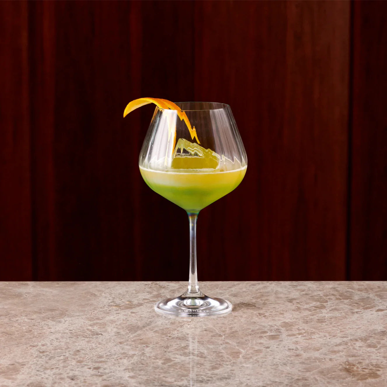 Manhattan cocktail served in a balloon glass with a vibrant green color and an orange twist garnish.